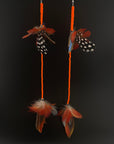 Two decorative earrings with feathers and orange beads on a black background