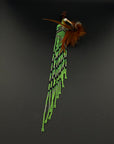 A South American style beaded brooch or pin featuring a turquoise stone, brown feathers, and long strands of green, black, and white beads, displayed on a dark gray background.