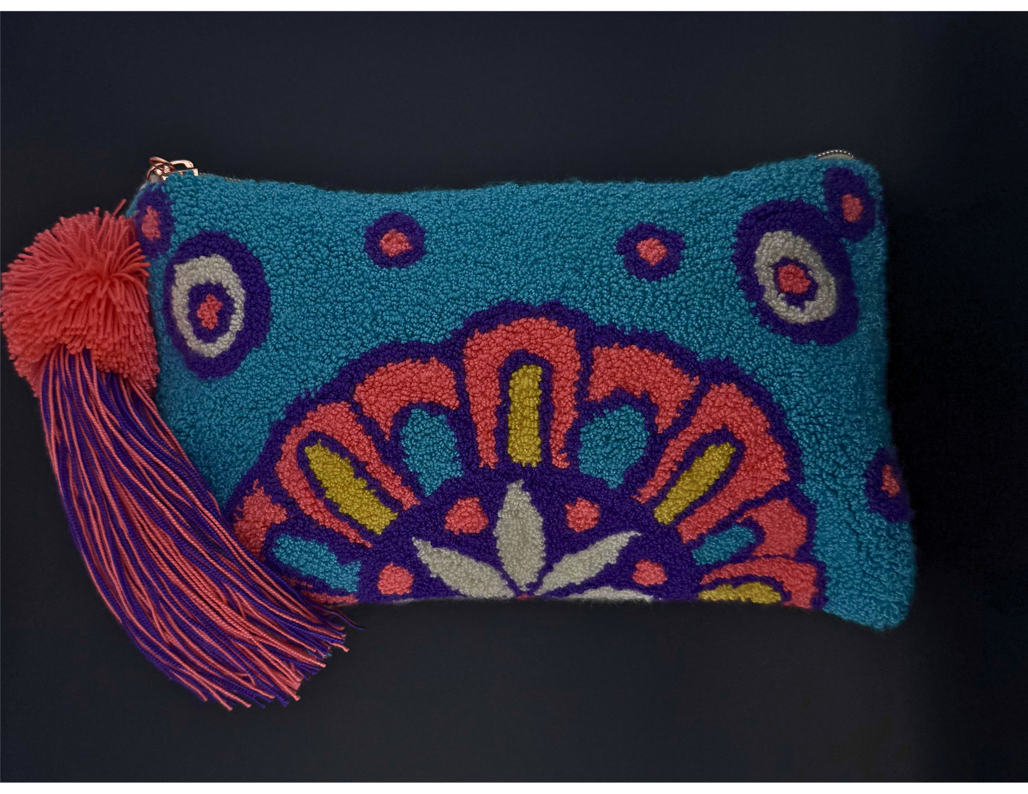 A turquoise blue hook-and-loop pouch with a colorful mandala pattern in orange, purple, yellow, and white, featuring a red pom-pom and tassel zipper pull on a black background.