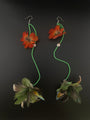 Pair of earrings with orange flowers and green beads on a dark background