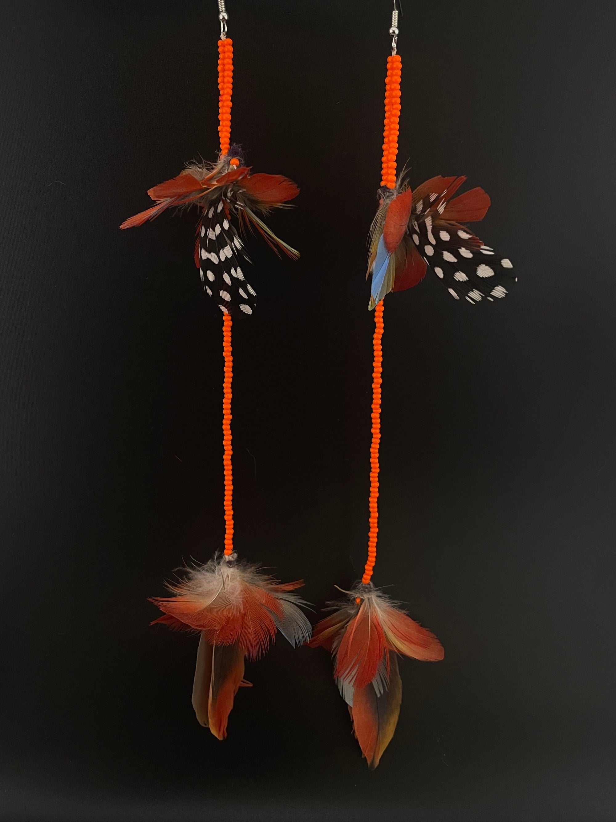 Two decorative earrings with feathers and orange beads on a black background