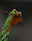 A South American style beaded brooch or pin featuring a turquoise stone, brown feathers, and long strands of green, black, and white beads, displayed on a dark gray background.